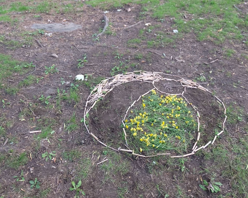 Sur un sol gazonné, reproduction d'un ballon de plage en deux dimensions, fait avec des petits batonnets et des fleurs