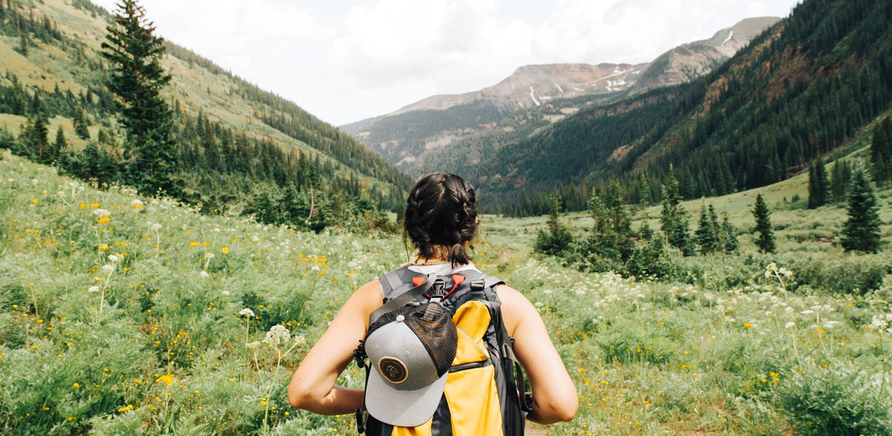 Femme de dos portant un sac-à-dos dans une grande vallée bordée de montagnes